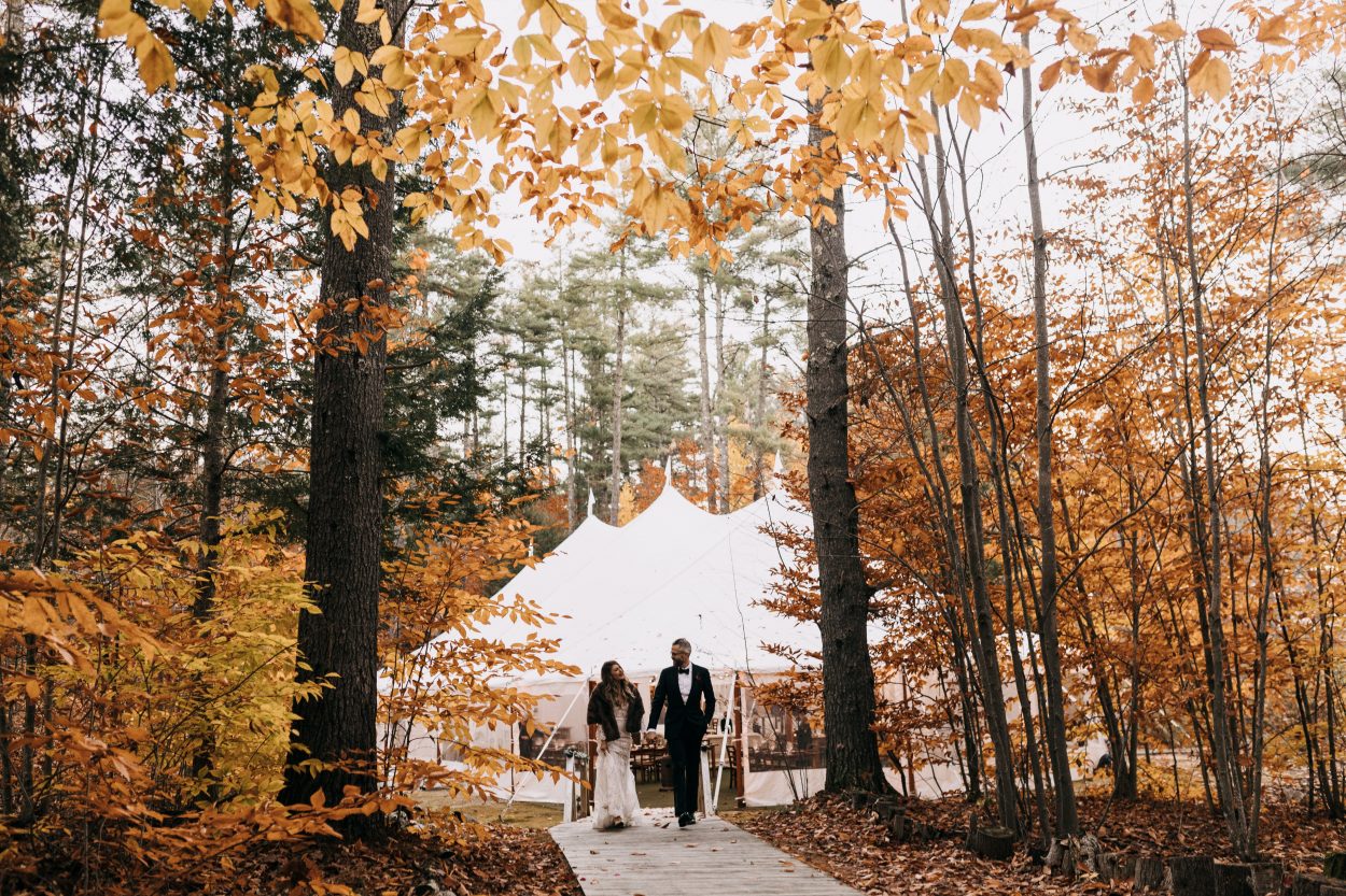 Bride and groom walking by tent in the fall